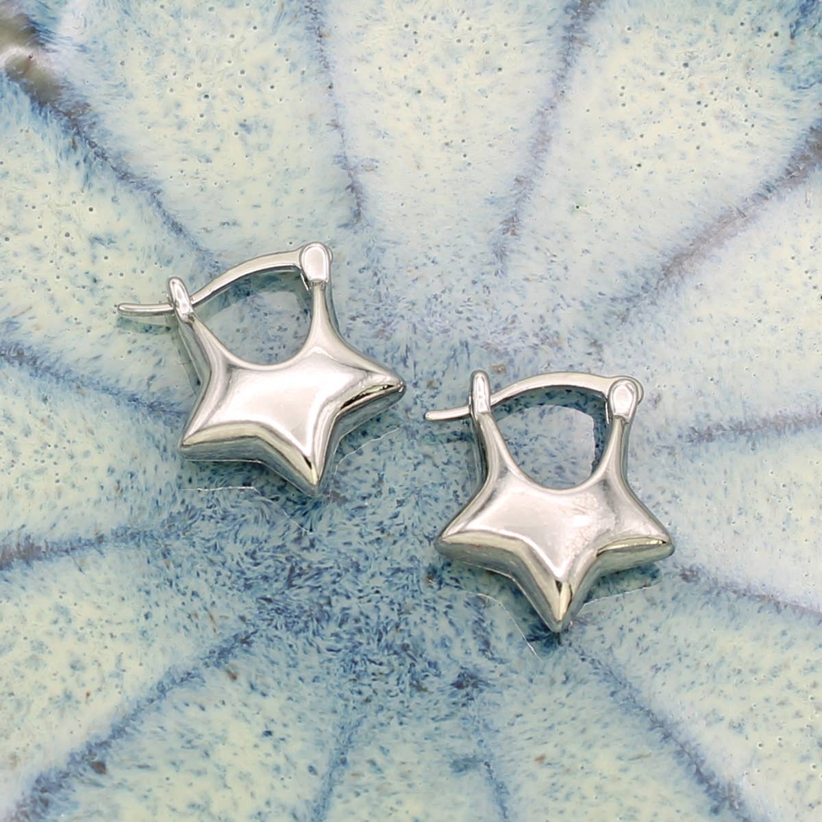 Pair of silver star-shaped earrings on a textured blue and white background.