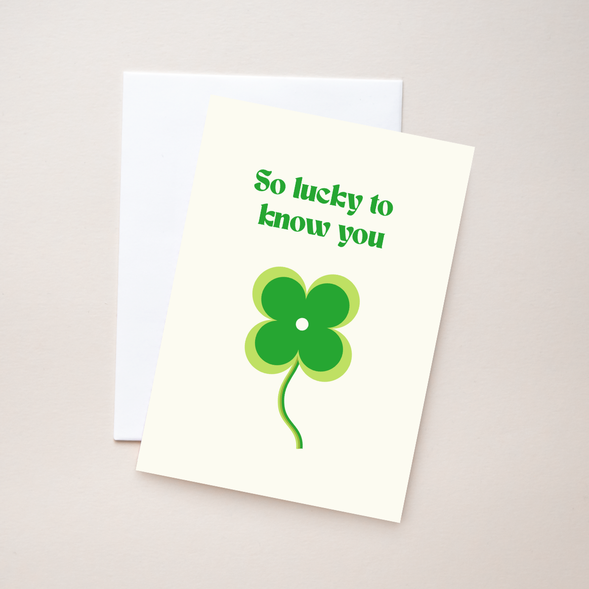 Greeting card with text "So lucky to know you" on an off white card with green text, white envelope, on a beige background.